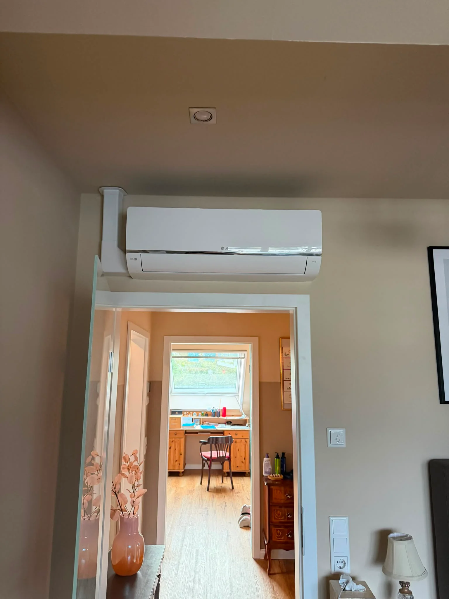 LG-Dual-Inverter-Innengerät weiß über einem Türrahmen im Übergang zwischen zwei Wohnräumen, mit weißem Installationskanal an der Wand