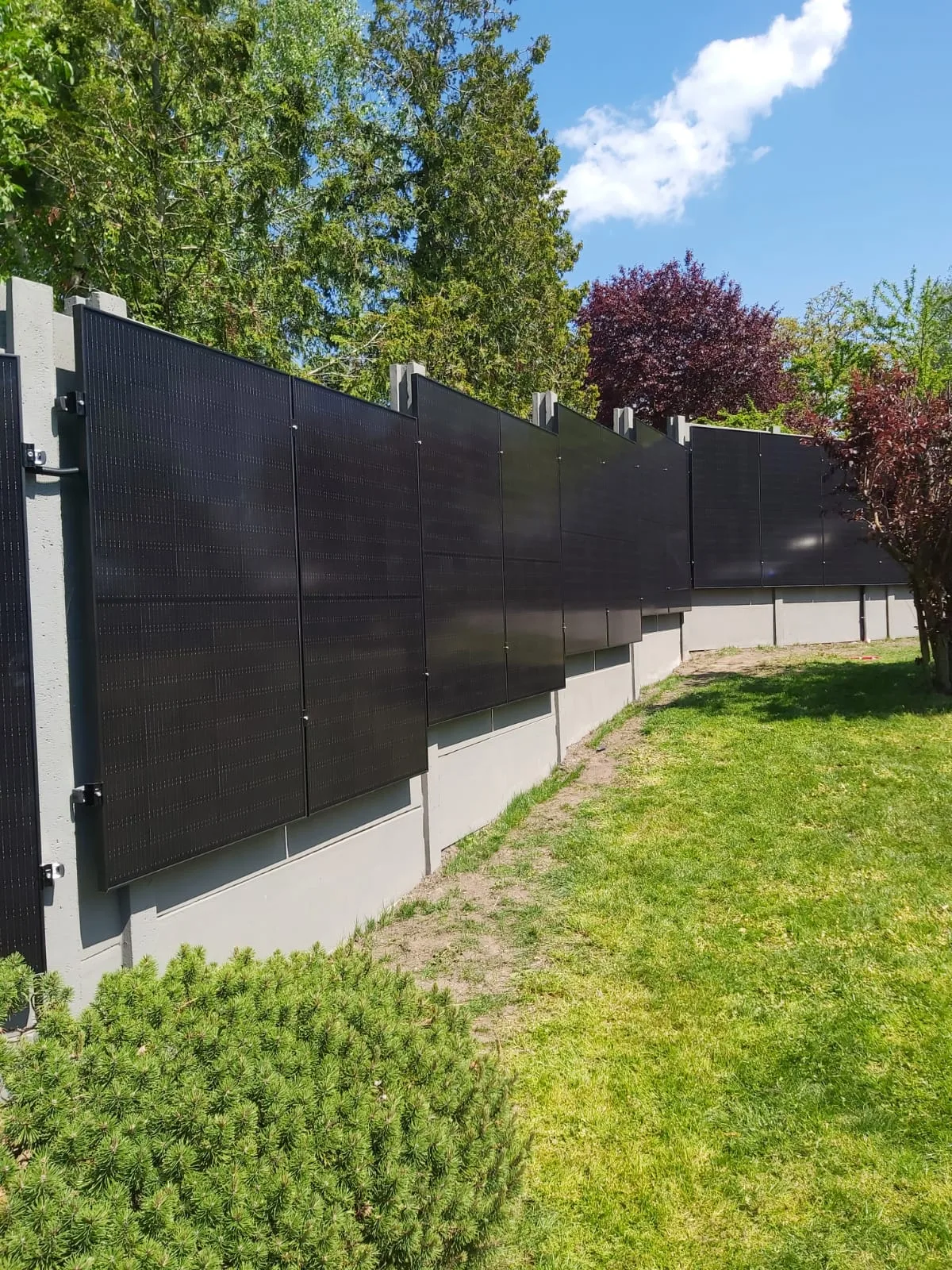 Bestehender Betonzaun in einem Garten mit hochkant montierten schwarzen Full-Black-Photovoltaikmodulen an der Sonnenseite