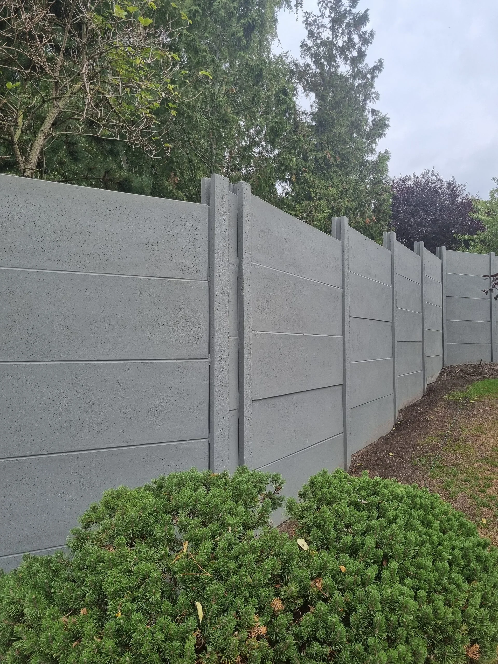 Bestehender grauer Betonzaun mit vertikalen Pfeilern im Garten vor Beginn der Photovoltaik-Nachrüstung