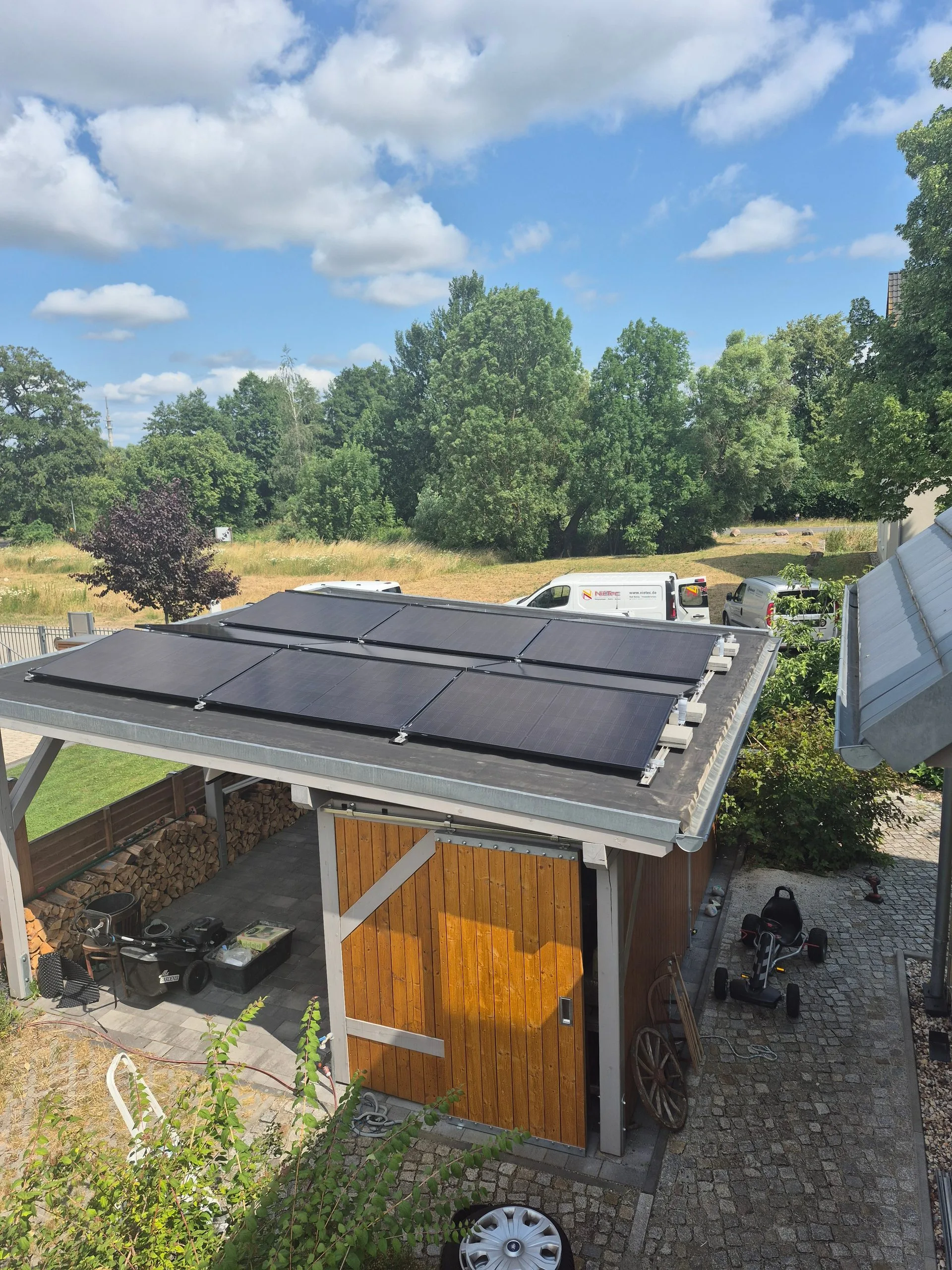 Aufgeständerte Photovoltaikmodule auf dem Flachdach eines Carports, im Hintergrund grüne Wiese und Bäume