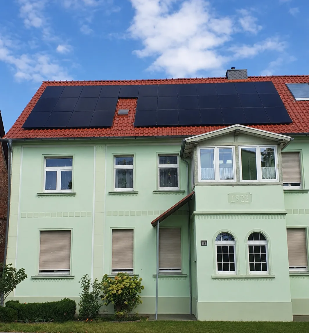 Historisches Wohnhaus in Hohenwerbig mit grüner Putzfassade und Giebeljahr 1922: dachparallel montierte schwarze Solar Fabrik S3 HalfCut Full-Black-Module auf dem roten Ziegeldach
