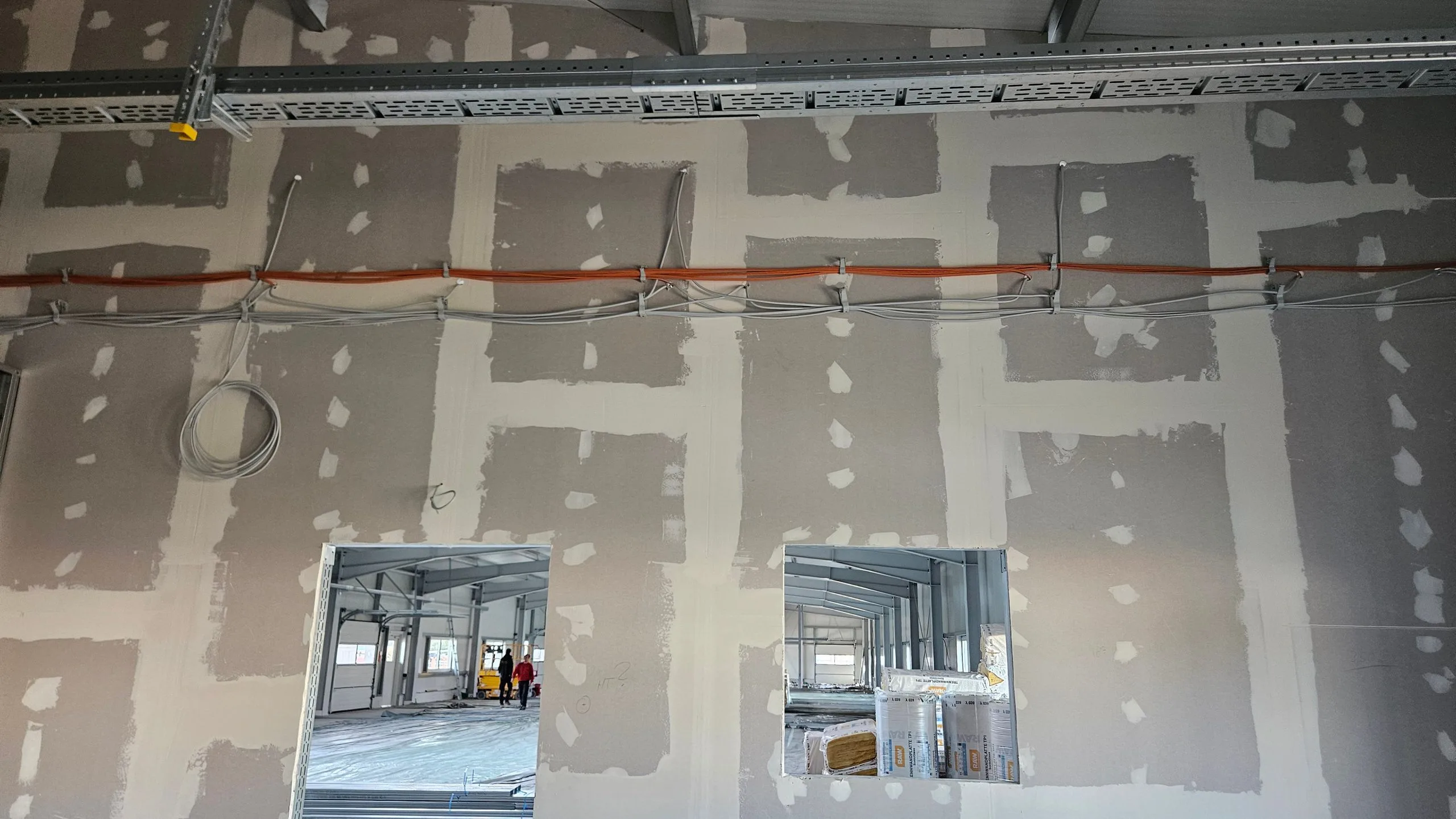 Kabeltrasse mit orangen und weißen Leitungen entlang einer verspachtelten Trockenbauwand während der Rohinstallation