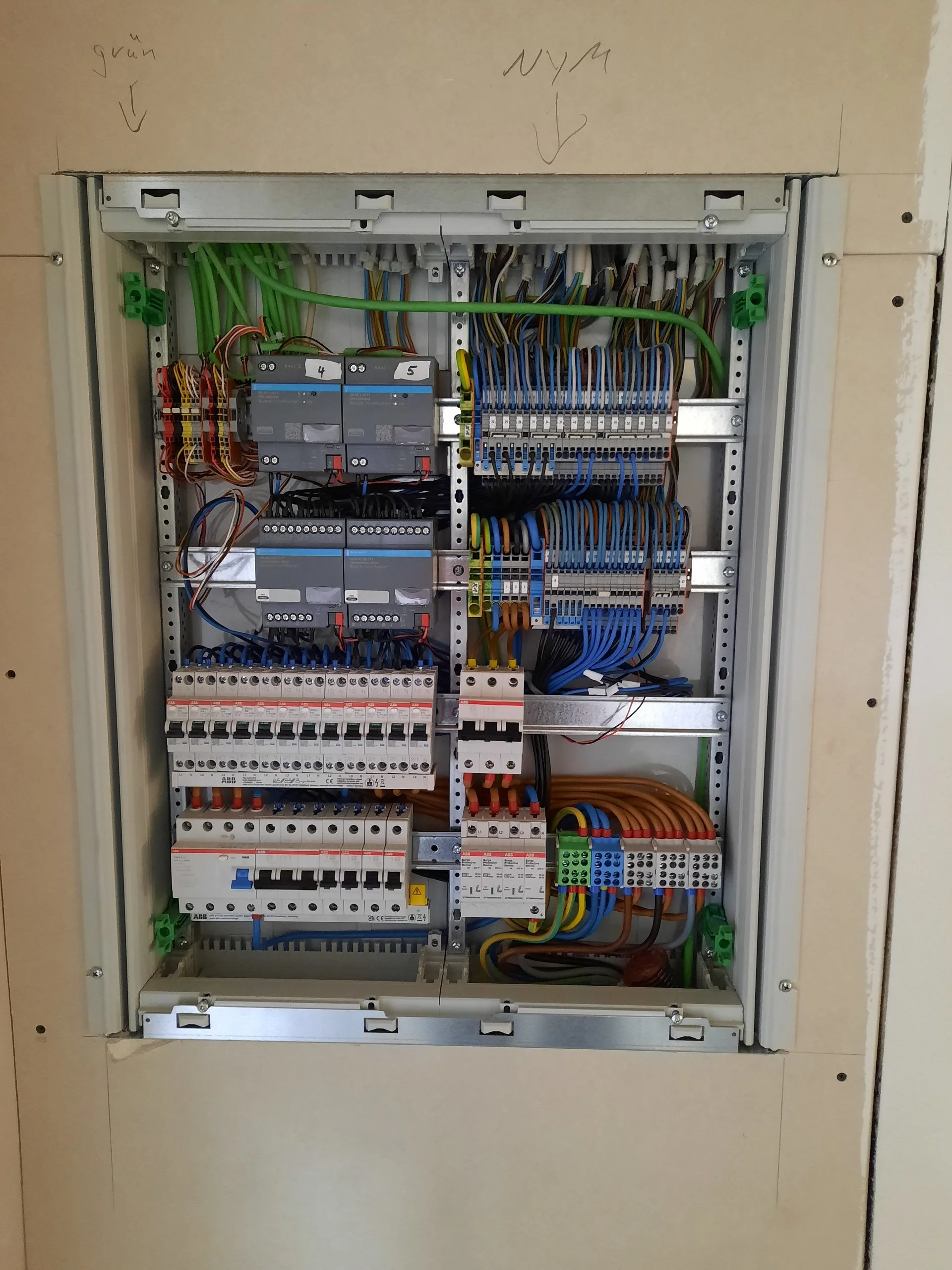 Detail einer Elektroverteilung: zwei Bus-Gateways mit den Nummern 4 und 5, mehrere Reihen ABB-Leitungsschutzschalter, ein Fehlerstromschutzschalter und rot markierte Überspannungsableiter mit sauber verlegten blauen und braunen Adern