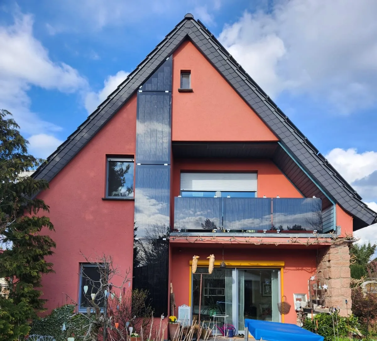 Wohnhaus mit rosafarbener Putzfassade und dunklem Ziegeldach in Treuenbrietzen: sieben senkrecht montierte Photovoltaikmodule an der Giebelseite neben dem Balkon