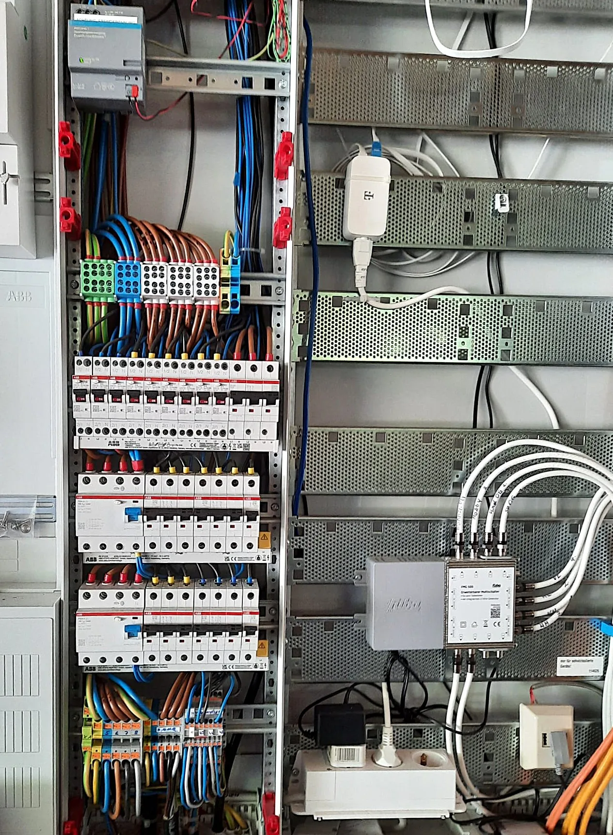 Detailaufnahme einer geöffneten Unterverteilung mit ABB-Reiheneinbaugeräten, Fehlerstromschutzschaltern, farbig sortierten Adern und einem Multischalter der Satellitenanlage in einem Einfamilienhaus-Neubau in Wiesenburg (Mark)